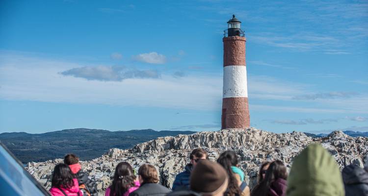 Groupe de personnes observant un phare sur une île rocheuse.