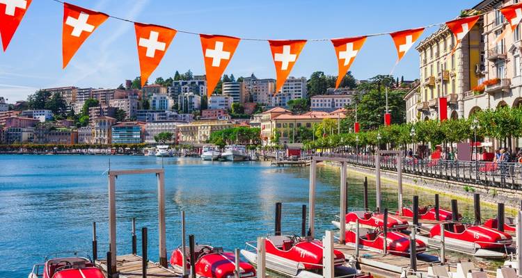 A pristine lakeside city with Swiss flags and boats.