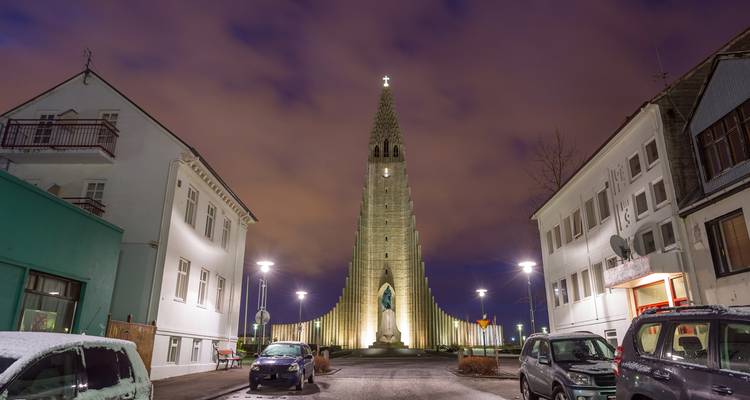 Vue nocturne de l'église Hallgrímskirkja illuminée dominant une rue tranquille de Reykjavik.
