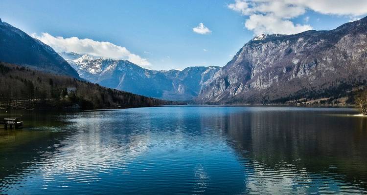 Crystal-clear alpine lake reflects surrounding snow-tipped peaks and wooded slopes.