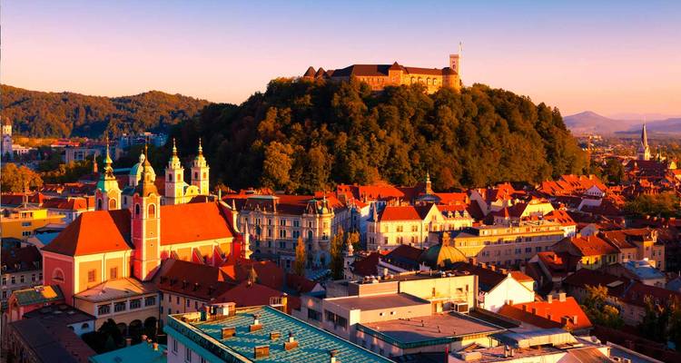 Stadtlandschaft mit einem Schloss auf einem Hügel bei Sonnenuntergang.