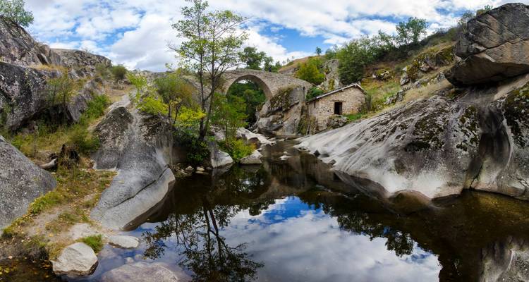 Vue panoramique d'un ancien pont de pierre enjambant un ruisseau sous un ciel dramatique.
