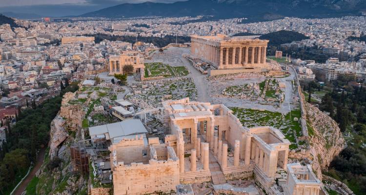 Vista aérea de la Acrópolis de Atenas y el paisaje urbano circundante durante el atardecer.