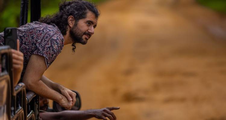 Ein Mann, der sich aus einem Safari-Fahrzeug lehnt und die Umgebung betrachtet, mit einem Feldweg vor ihm.