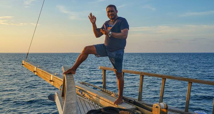 Ein Mann, der am Rand eines Bootes auf dem Meer steht und eine Geste macht.