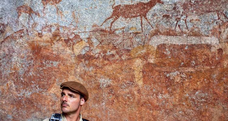 Un homme debout devant de l'art rupestre ancien représentant la faune.