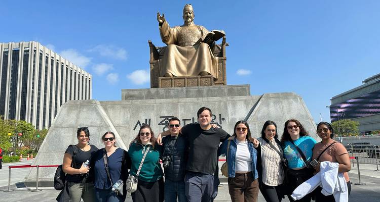 Grupo de pie frente a una gran estatua y monumento en una plaza de la ciudad.