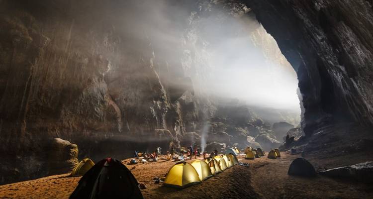 Un grupo de tiendas de campaña dentro de una cueva grande con luz que entra a raudales.