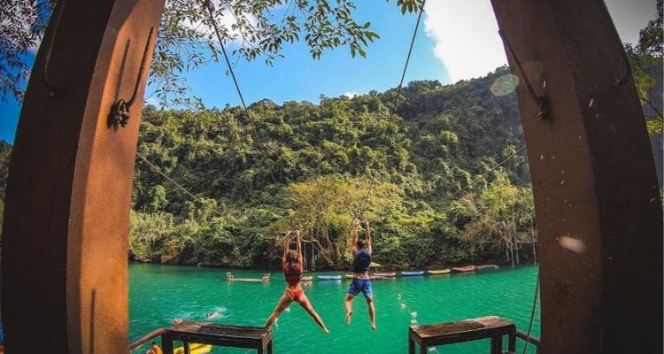 Personas balanceándose hacia una masa de agua rodeada de vegetación.