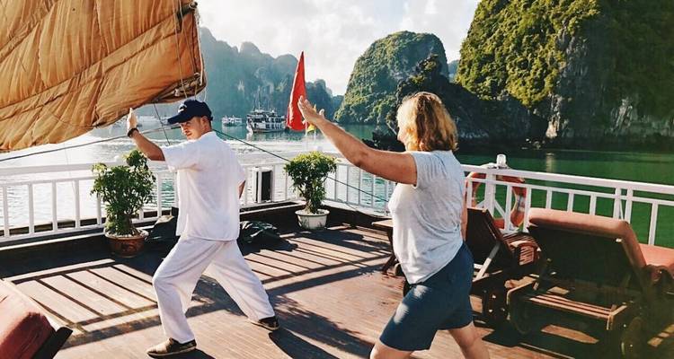 Gente practicando Tai Chi en un barco con rocas pintorescas.