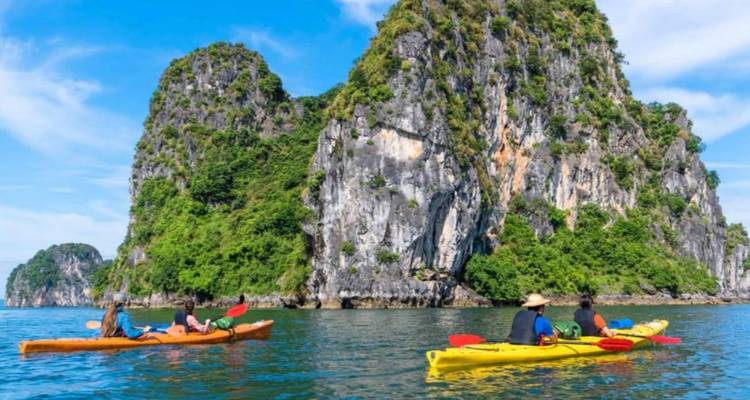 Personas navegando en kayak cerca de grandes montañas de piedra caliza sobre agua cristalina.