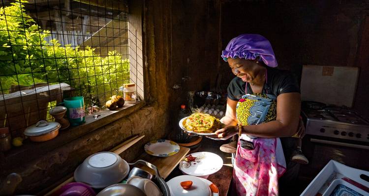 Vrouw in een keuken die een bord eten vasthoudt, glimlachend in het zonlicht.