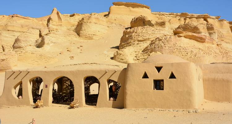 Structure en adobe aux tons terreux contre un décor de désert rocheux.