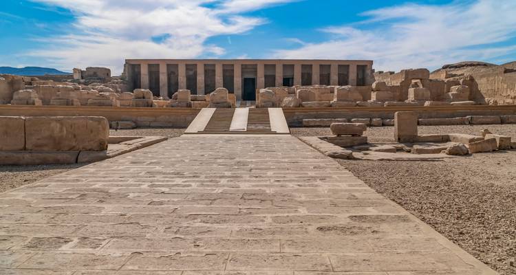 Un temple antique avec des colonnes et des ruines sous un ciel bleu.