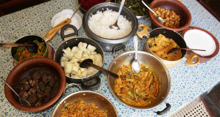 Assortiment van traditionele Sri Lankaanse curry's, rijst en bijgerechten uitgestald in diverse klei- en metalen potten op een tafel.