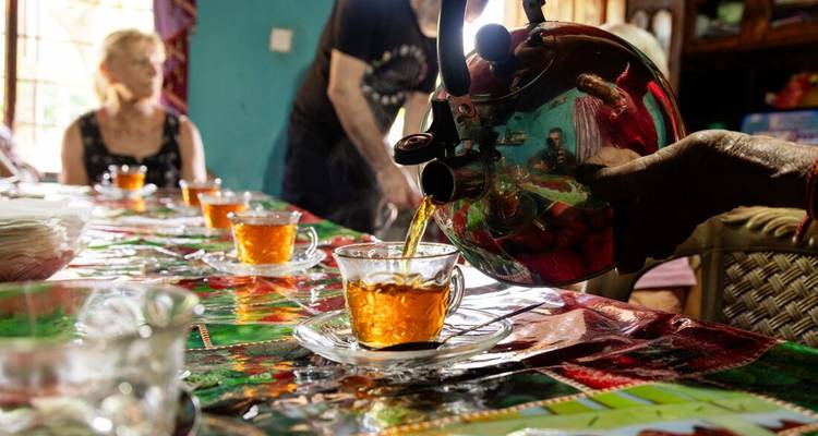 Thee die uit een ketel in glazen kopjes wordt geschonken op een kleurrijke tafel tijdens een lokaal bezoek