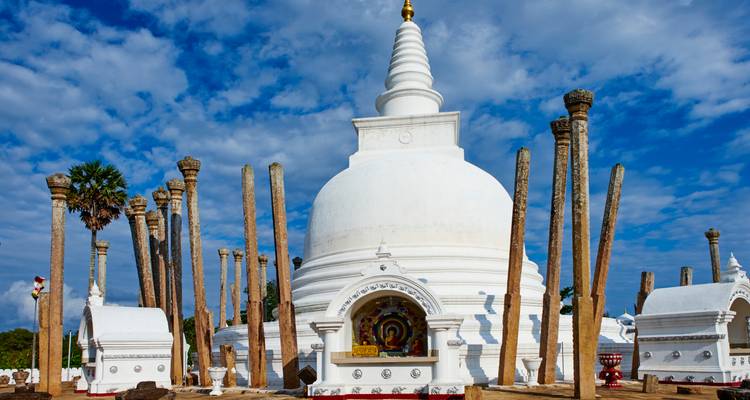 Dagoba blanc brillant entouré de hauts piliers de pierre sous un ciel bleu éclatant dans un site sacré ancien du Sri Lanka.