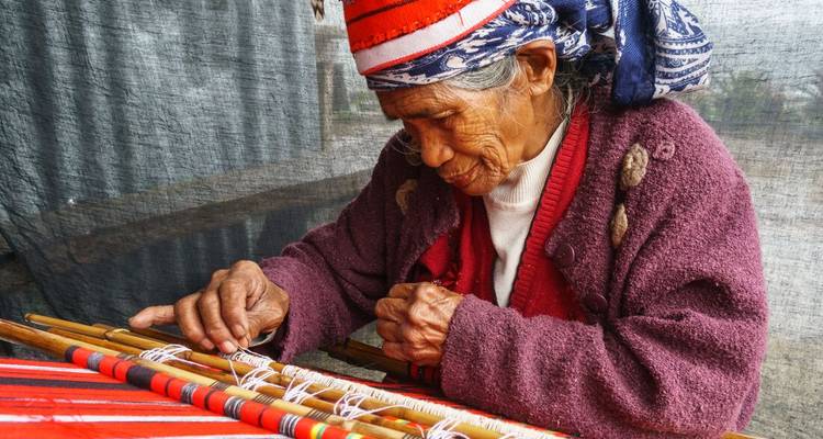 Une femme âgée pratique le tissage traditionnel en utilisant un métier à tisser manuel.