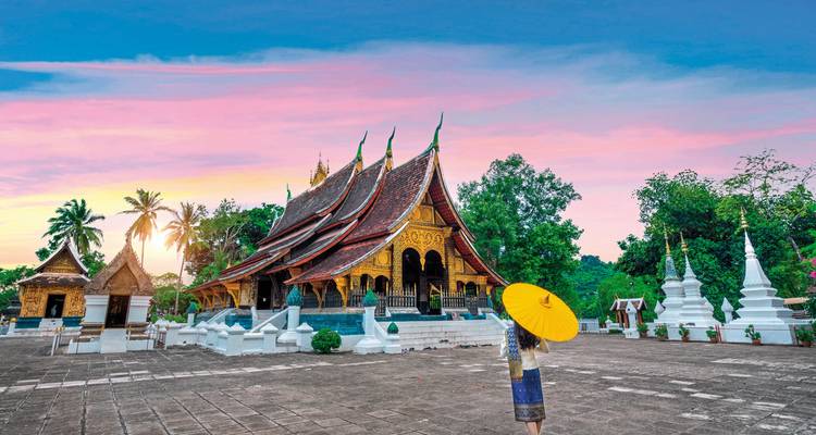 Woman holding an umbrella in front of a temple at sunrise.