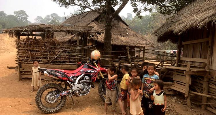 Kinderen die naast een motorfiets staan in een landelijke omgeving met traditionele hutten.