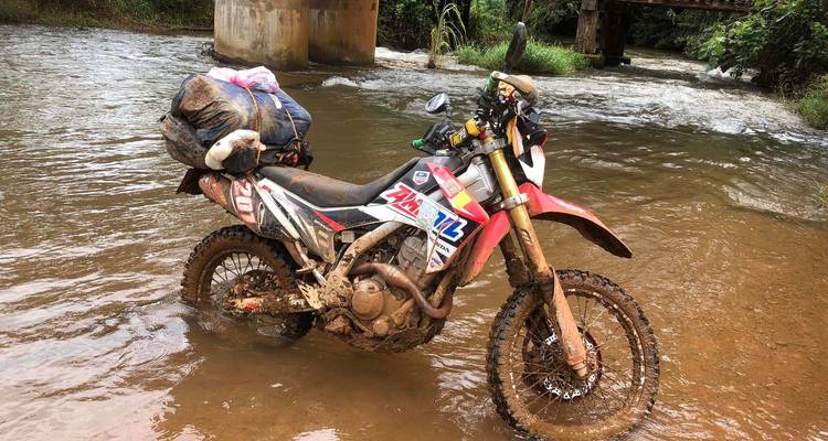 Een modderige crossmotor geparkeerd in een ondiepe rivier.