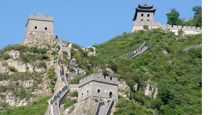 Steep mountain section of the Great Wall with two watchtowers rising above green slopes under a clear sky.
