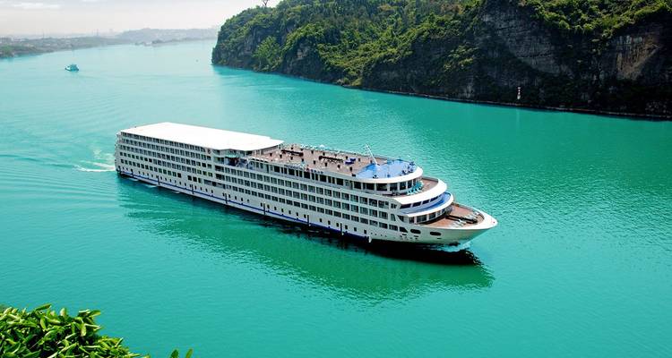 Crucero fluvial blanco de varios pisos navegando a través de aguas turquesas vibrantes entre acantilados verdes empinados.