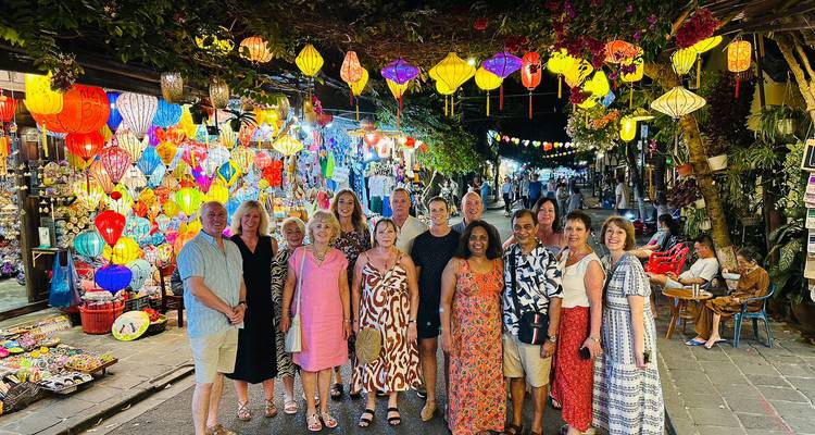 Large tour group poses beneath colourful lanterns on a bustling Hoi An night market street.