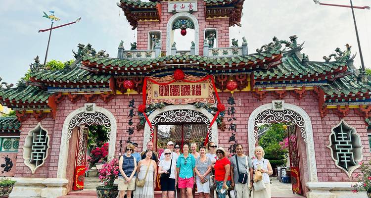 Travellers stand in front of an ornate Chinese assembly hall gate decorated with dragons and red signage in Hoi An.