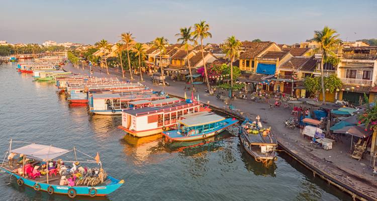 Colourful boats line the Thu Bon River along Hoi An’s charming waterfront in warm afternoon light.