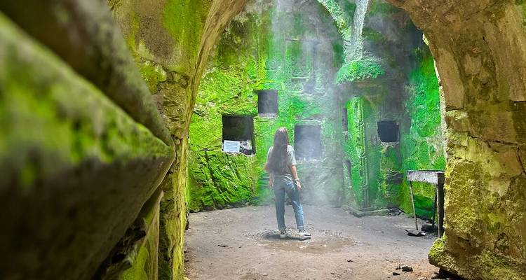 Personne explorant une grotte aux murs couverts de mousse verte.