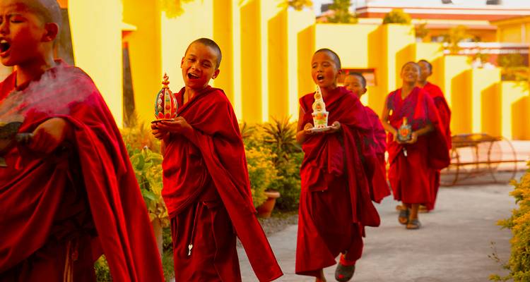 Groupe de jeunes moines en robes rouges marchant et portant des objets religieux.