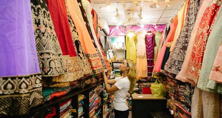 Comprador examinando vestidos tradicionales vibrantes en una tienda de textiles estrecha.
