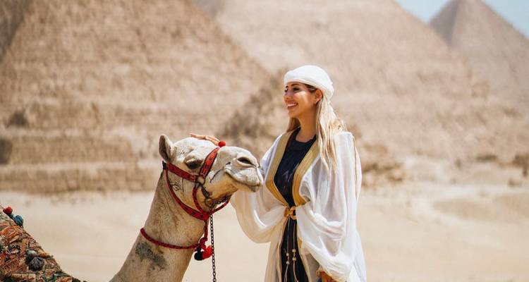 Persona en atuendo tradicional con un camello cerca de las pirámides.