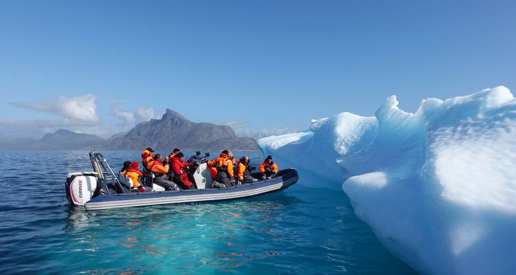 Touristen auf einem Boot erkunden eisige Gewässer in der Nähe eines Eisbergs.