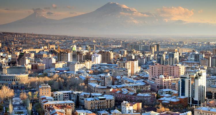 Panoramic view over Yerevan with Mount Ararat’s snow-capped peaks towering beyond the city in warm afternoon light.