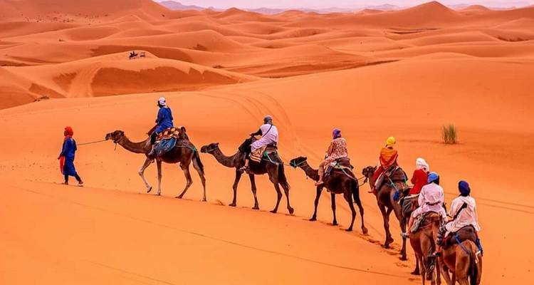 Menschen reiten auf Kamelen über Sanddünen in der Wüste.