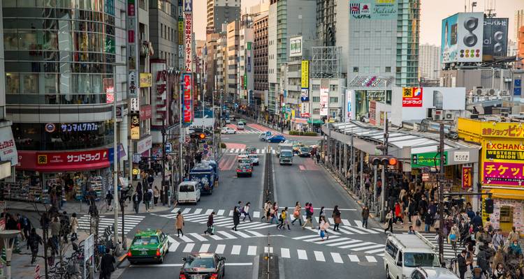 Animada calle urbana en Tokio con tráfico, letreros de neón y multitudes al atardecer
