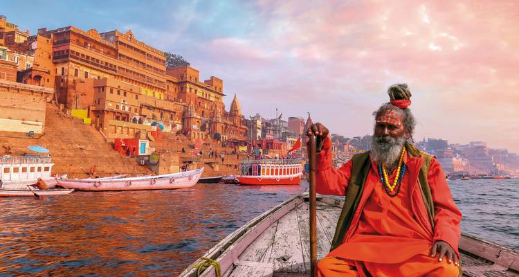 Een man in traditionele kleding op een boot in de Ganges rivier in Varanasi bij zonsopgang.