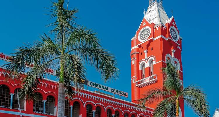 Rotes Gebäude mit Uhrenturm mit der Beschriftung Chennai Central, umgeben von Palmen.