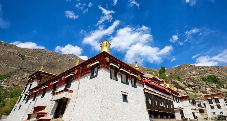 Whitewashed Tibetan monastery with gilded rooftop rises against a vivid blue sky.