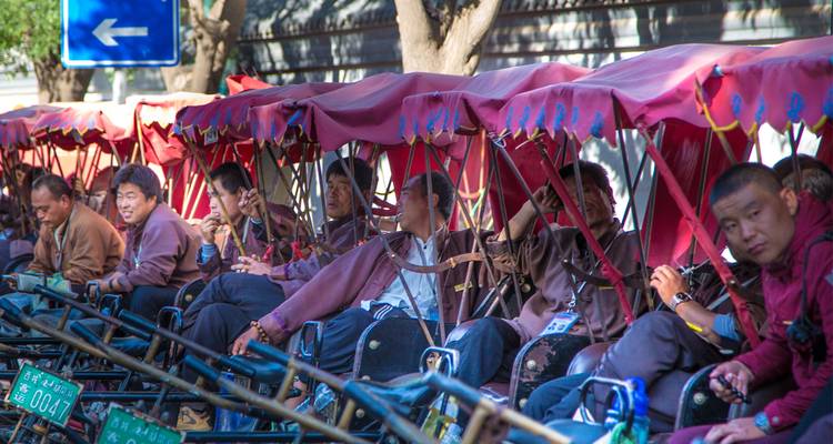 Eine Reihe von Rikschas mit Fahrern, die am Straßenrand warten.