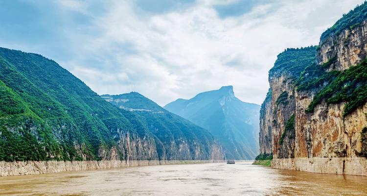 Wide river with steep forested cliffs under a cloudy sky.