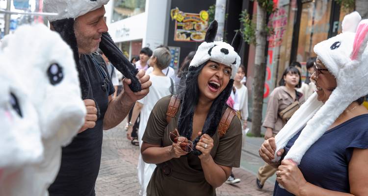 Los turistas se ríen mientras se prueban sombreros de animales divertidos en una acera de la ciudad.