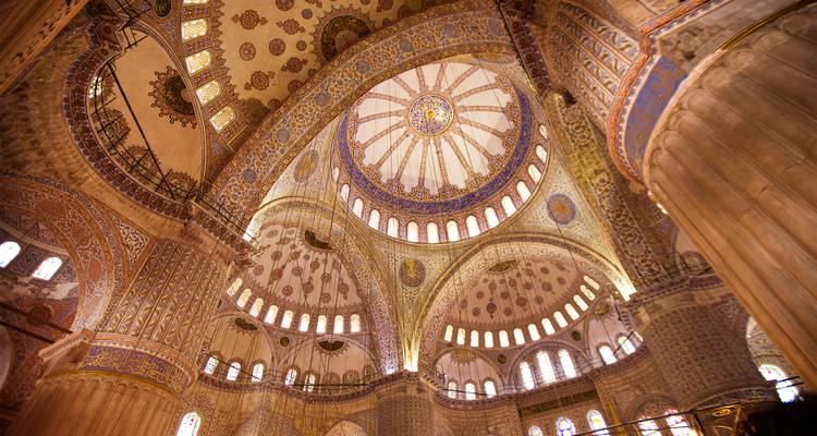 Interior lujoso de la Mezquita Azul con cúpulas ornamentadas, arcos y los intrincados patrones de azulejos de Iznik iluminados por la luz natural.