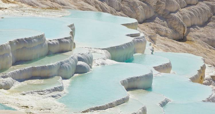 Impresionantes terrazas de piedra caliza blanca llenas de agua termal color turquesa que baja en cascada por la ladera de una montaña.