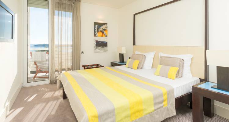 Habitación de hotel moderna y luminosa con ropa de cama a rayas amarillas y vista al mar desde el balcón.
