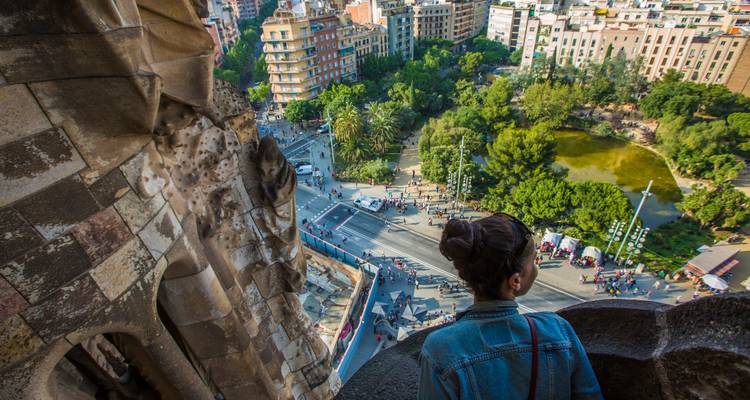Un visiteur regarde par une ouverture élevée de la tour de la Sagrada Família surplombant les rues et le parc de Barcelone en contrebas.