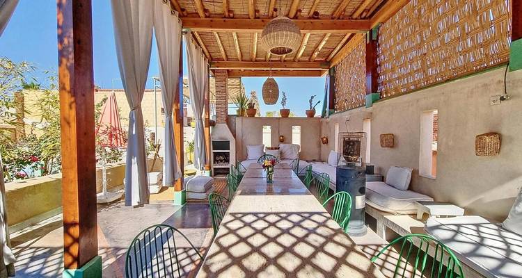Répétition de la prise de vue de la terrasse lumineuse du riad avec table longue et banquettes rembourrées.