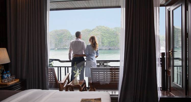 Couple debout sur le balcon d'un bateau surplombant une baie avec des îles.
